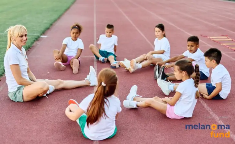 Coach or PE teacher sitting in a circle with with a group of young children on an outdoor athletics track