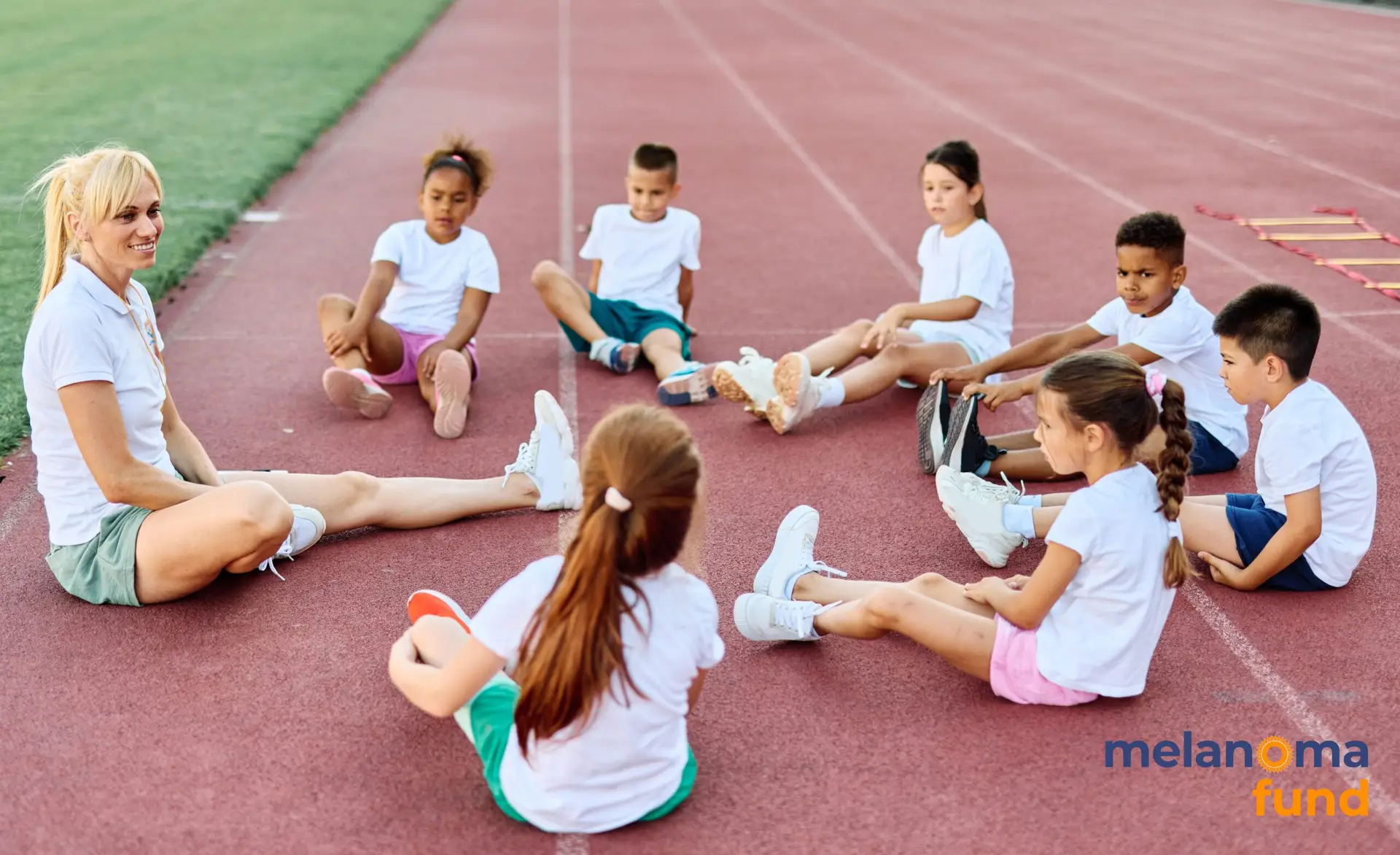 Coach or PE teacher sitting in a circle with with a group of young children on an outdoor athletics track
