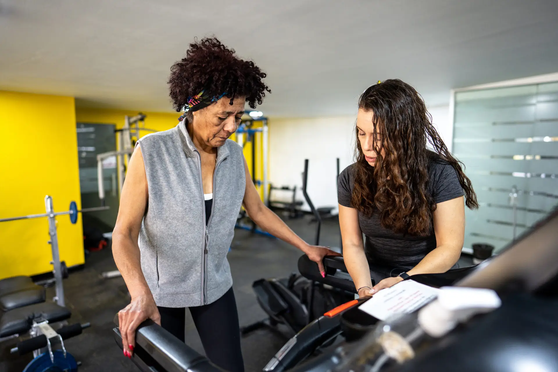 Female fitness instructor helping senior woman on treadmill in the gym