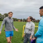 Small group of coaches standing a pitch. They are setting up equipment talking together, talking while waiting for their team.