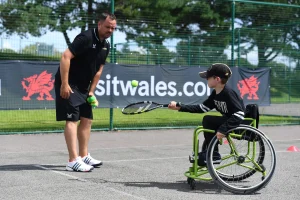 Coach supporting a participant using a wheelchair with tennis techniques in Wales